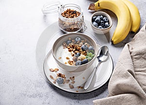 Muesli with vegetarian yogurt, banana and blueberries in a bowl on a gray texture background. Healthy and dietary homemade granola