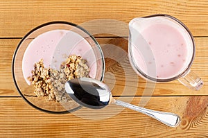 Muesli with yogurt in bowl, spoon, pitcher with yogurt on wooden table. Top view