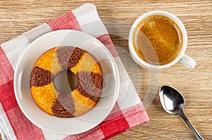 Muffin in shape ring in white saucer on napkin, cup with coffee espresso, spoon on table. Top view