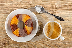 Muffin in shape ring in white saucer, spoon, cup with coffee on wooden table. Top view