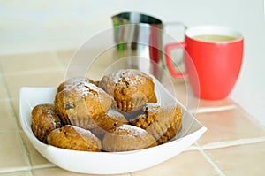 Muffins with powdered sugar on a platter and a milk pitcher with a mug