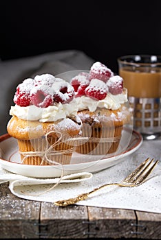 Muffins with soft cream and fresh raspberry powdered with sugar, cup of coffee with milk, rustic background
