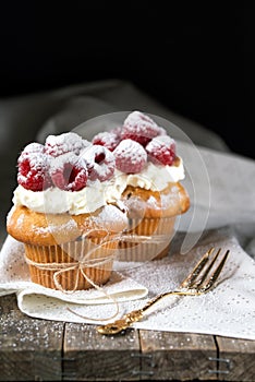 Muffins with soft cream and fresh raspberry powdered with sugar, rustic background