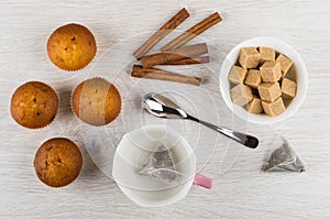 Muffins, teabag in cup, sugar, cinnamon sticks, teaspoon on table