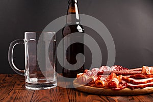 Mug of beer and assortment of snacks on a wooden table. Sausage, salami, ham, bacon. Beer salty snack, chips, wasabi nuts, salted