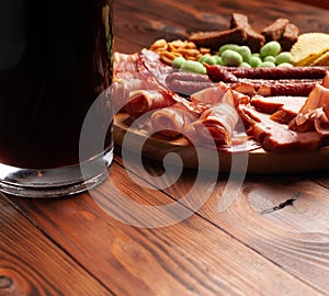 Mug of beer and assortment of snacks on a wooden table. Sausage, salami, ham, bacon. Beer salty snack, chips, wasabi nuts, salted
