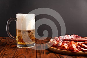 Mug of beer and assortment of snacks on a wooden table. Sausage, salami, ham, bacon. Beer salty snack, chips, wasabi nuts, salted