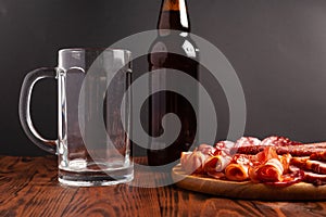 Mug of beer and assortment of snacks on a wooden table. Sausage, salami, ham, bacon. Beer salty snack, chips, wasabi nuts, salted