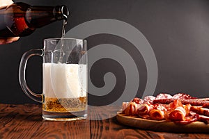 Mug of beer and assortment of snacks on a wooden table. Sausage, salami, ham, bacon. Beer salty snack, chips, wasabi nuts, salted