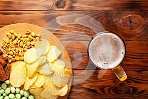 Mug of beer and assortment of snacks on a wooden table. Sausage, salami, ham, bacon. Beer salty snack, chips, wasabi nuts, salted