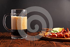 Mug of beer and assortment of snacks on a wooden table. Sausage, salami, ham, bacon. Beer salty snack, chips, wasabi nuts, salted