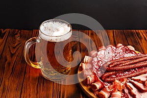 Mug of beer and assortment of snacks on a wooden table. Sausage, salami, ham, bacon. Beer salty snack, chips, wasabi nuts, salted