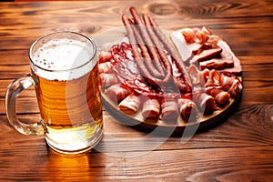 Mug of beer and assortment of snacks on a wooden table. Sausage, salami, ham, bacon. Beer salty snack, chips, wasabi nuts, salted