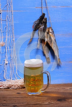 Mug of beer on blue background with dried rudd fish