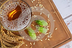 Mug with beer, fresh hops and ears of wheat on white wooden table, top view. Space for text