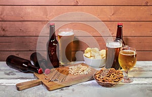 Mug of beer, glasses of beer, beer bottles and beer snacks on aged wooden table