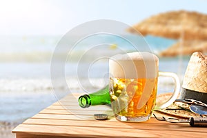 Mug of beer on table on beach with straw umbrellas