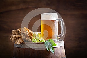 Mug of beer, wheat ears and green hops on a wooden barrel