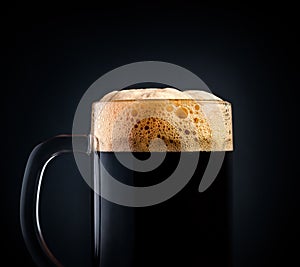 Mug of black beer or kvass on a black background. Foam close-up. Stock photo