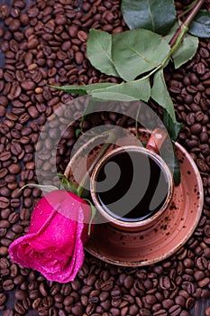 Mug of black coffee and rose on roasted coffee beans