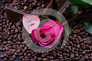 Mug of black coffee and rose on roasted coffee beans