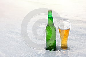 Mug and bottle of cold beer in the snow at sunset. Beautiful winter background. Outdoor recreation.