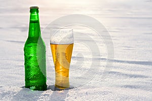Mug and bottle of cold beer in the snow at sunset. Beautiful winter background. Outdoor recreation.