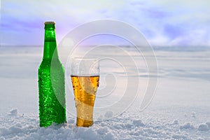 Mug and bottle of cold beer in the snow at sunset. Beautiful winter background. Outdoor recreation.