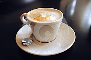 A mug of cappuccino on a saucer stands on a dark table macro photo.