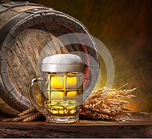 Mug of chilled beer, wheat ears and wooden beer cask on the wooden table