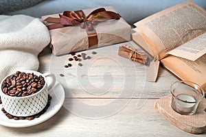 A mug with coffee beans, a gift box, a book, a sweater on a wooden table, with space for copying.