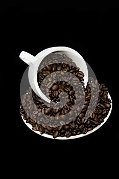 Mug of coffee beans with saucer on black background.