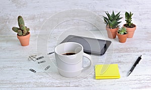 mug of coffee on a desk with pen and note paper clip and cactus