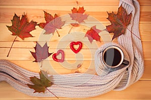 Mug of coffee, gray scarf, autumn leaves and two red hearts on wooden table