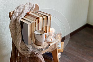 Mug with coffee and home decor on wooden chair. Warm sweater old books, candles, seasonal fall autumn winter weekend concept, copy