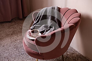 Mug of coffee with knitted sweater stay in accent chair in room closeup. Good morning. Breakfast