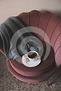 Mug of coffee with knitted sweater stay in accent chair in room closeup. Good morning. Breakfast