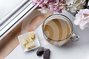 Mug of coffee with milk, chocolates, pieces of cheese, hydrangea flowers near the window
