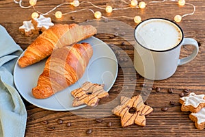 A mug of coffee with milk and foam, latte, cappuccino on a wooden table next to a fresh croissant and New Year`s garlands. Festiv