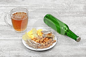 Mug of cold beer, bottle and snacks on the light wooden background. Chips, croutons, salted fish and peanuts.