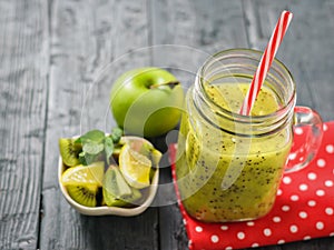 Mug with freshly made kiwi smoothie on a red rag and apple and lemon on a rustic black table.