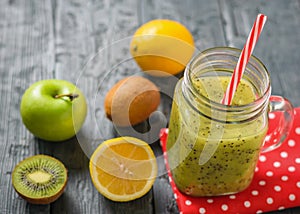 Mug with freshly made kiwi smoothie on a red rag and parsley and apple on a rustic wooden black table.