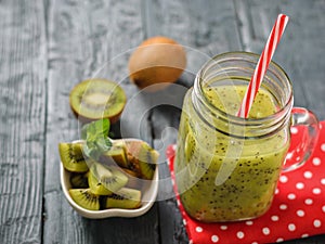 Mug with freshly made kiwi smoothie on a red rag and parsley on a rustic wooden black table.