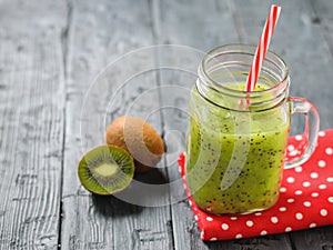 Mug with freshly made kiwi smoothie on a red rag on a rustic wooden table.