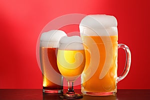 Mug and glass of beer close-up with froth over red background