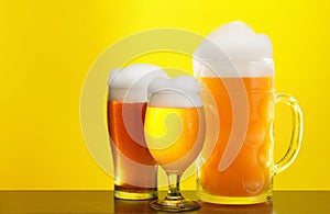 Mug and glass of beer close-up with froth over yellow background
