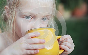 A mug in hands of child. Girl drinking something. Child outdoors in nature.