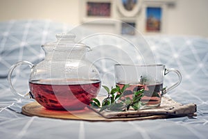 A mug of herbal tea and glass teapot on a wooden tray on the bed. Breakfast concept. Close up