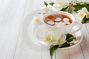 Mug of herbal tea with petals of Jasmine flowers on a light back