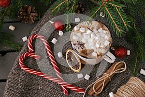 Mug of hot chocolate with marshmallow, fir branches, Lollipop, cone, red balls, anise, rope, cinnamon on a dark background, winter